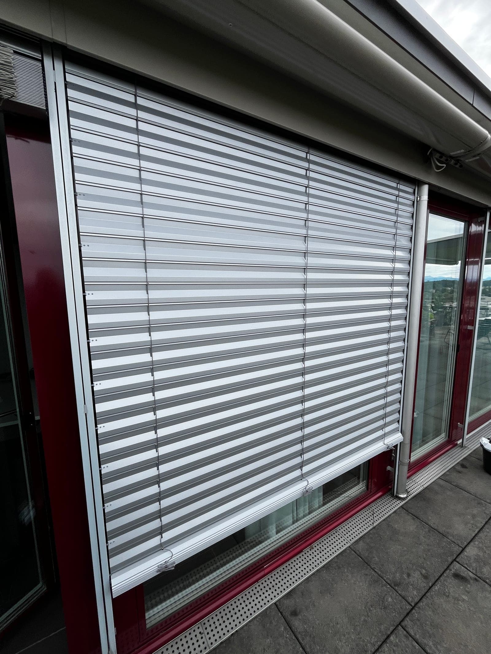 Silberfarbene Lamellenstore an einer Fensterfront