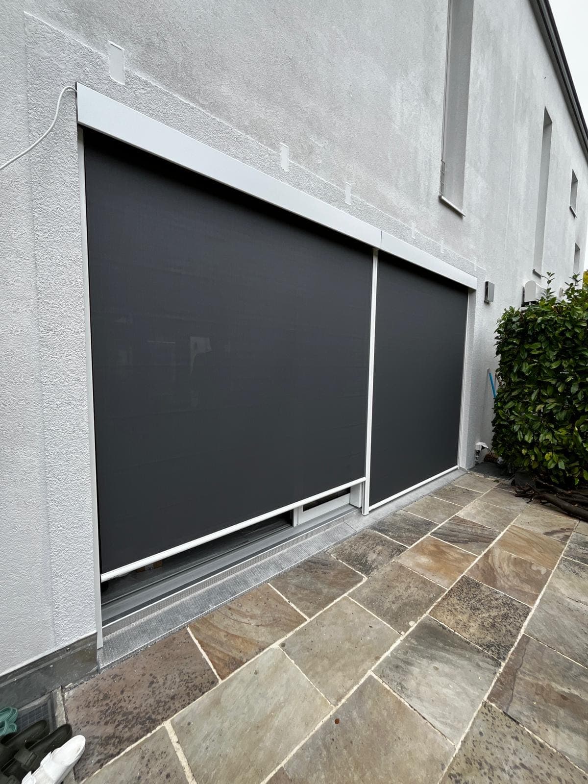 Zwei dunkle Senkrechtmarkisen vor grossen Fensterflächen an einer hellen, modernen Fassade