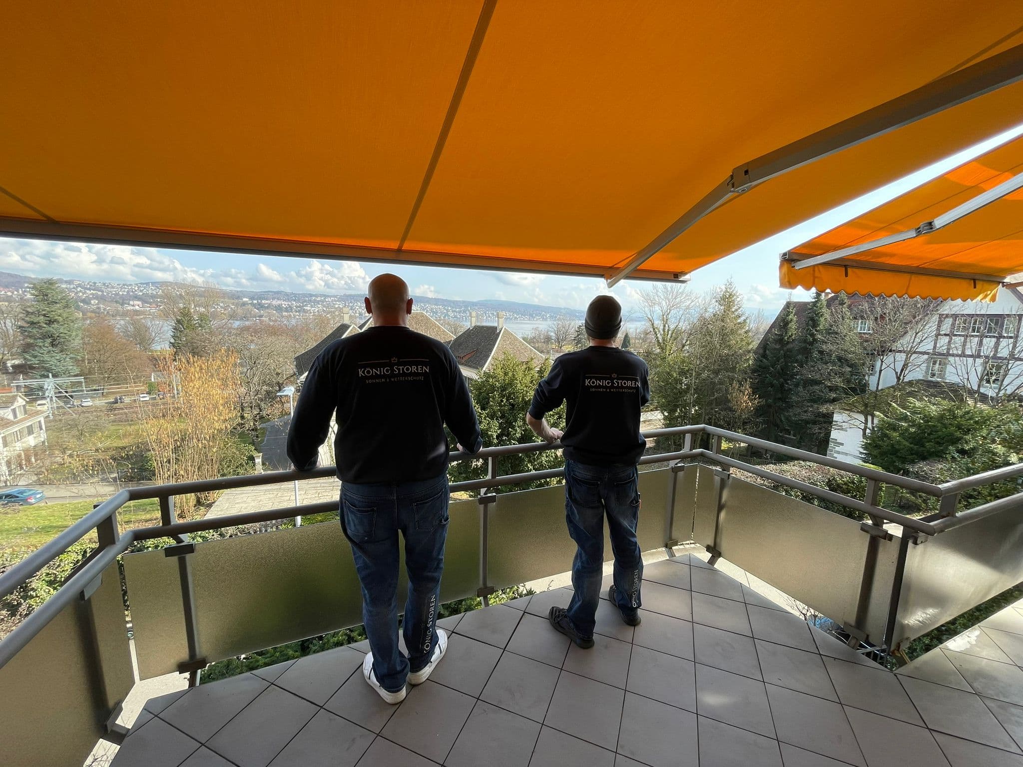 Ausgefahrene orange Sonnenstore über einem Balkon mit Blick ins Grüne